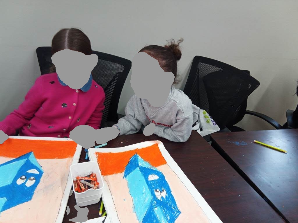 Two girls working on colorful oil pastel drawings at a table